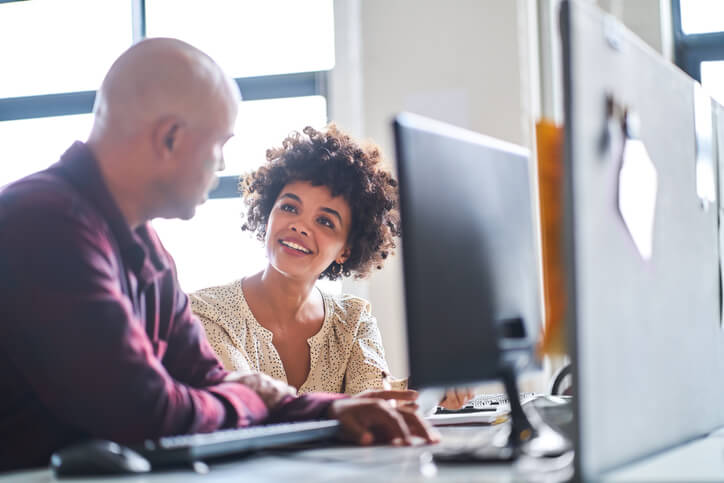 Mid adult businesswoman discussing with mature colleague. Male and female executives are sitting at computer desk. They are planning in office.